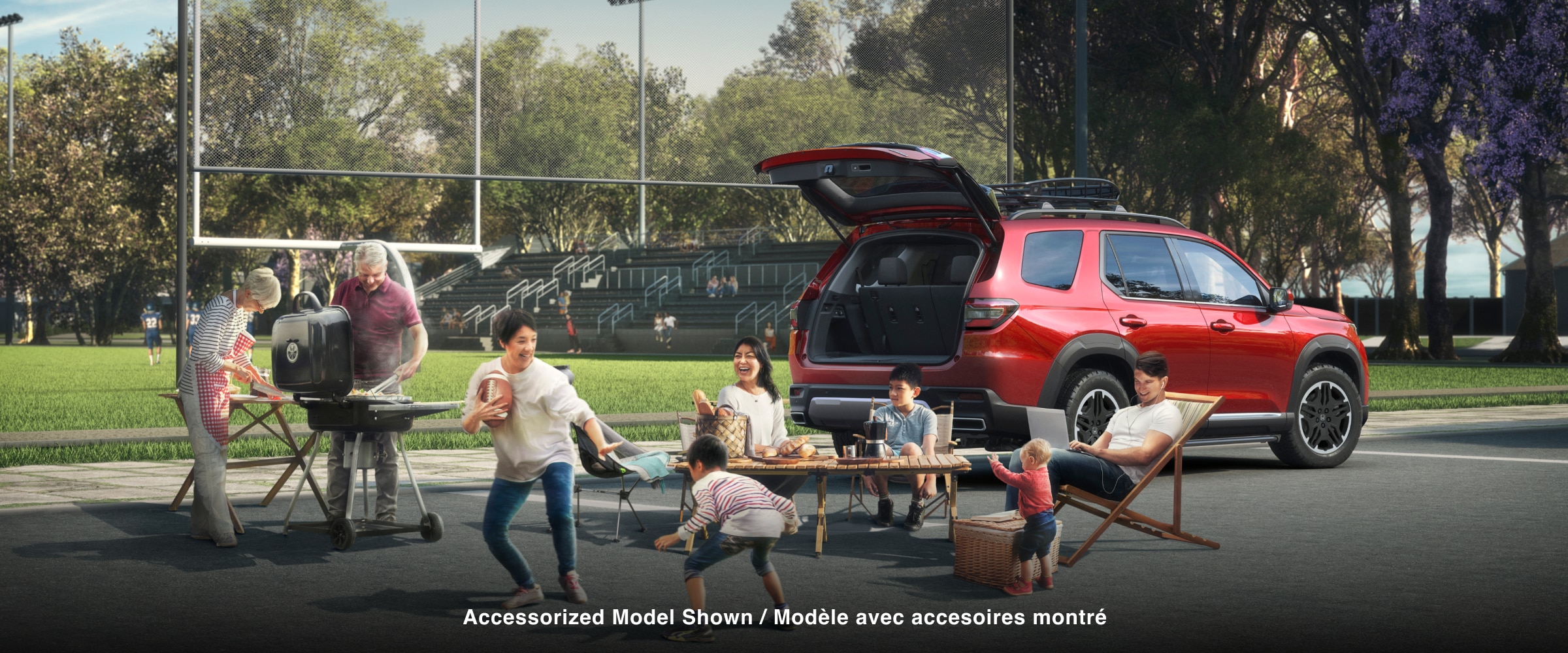 3/4 rear side view of a red Pilot parked at a sports field with its trunk open. Nearby, an older couple barbecues, a parent and child play with a football, and a family is sits at a folding table with a picnic basket.