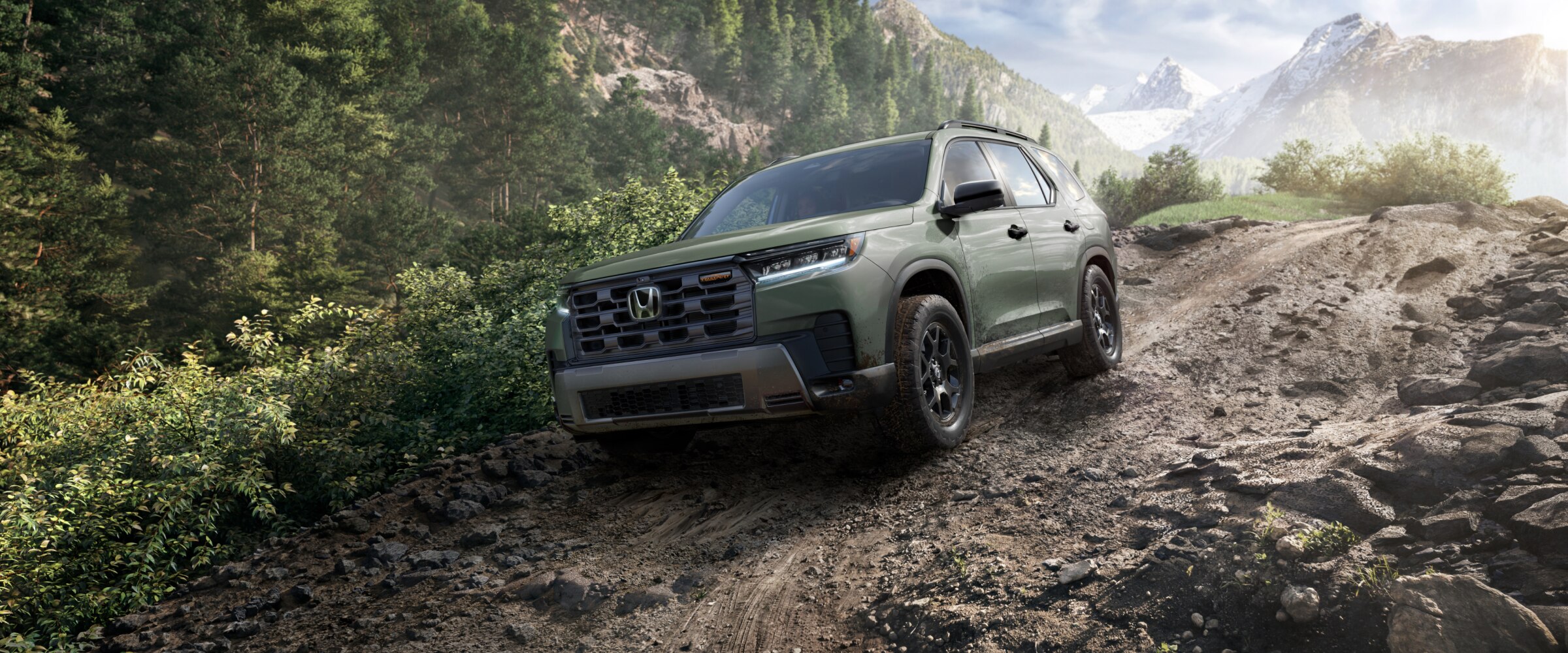 Vue de trois quarts avant d’un Pilot vert descendant un chemin de terre dans la forêt, avec des montagnes lointaines en arrière-plan.