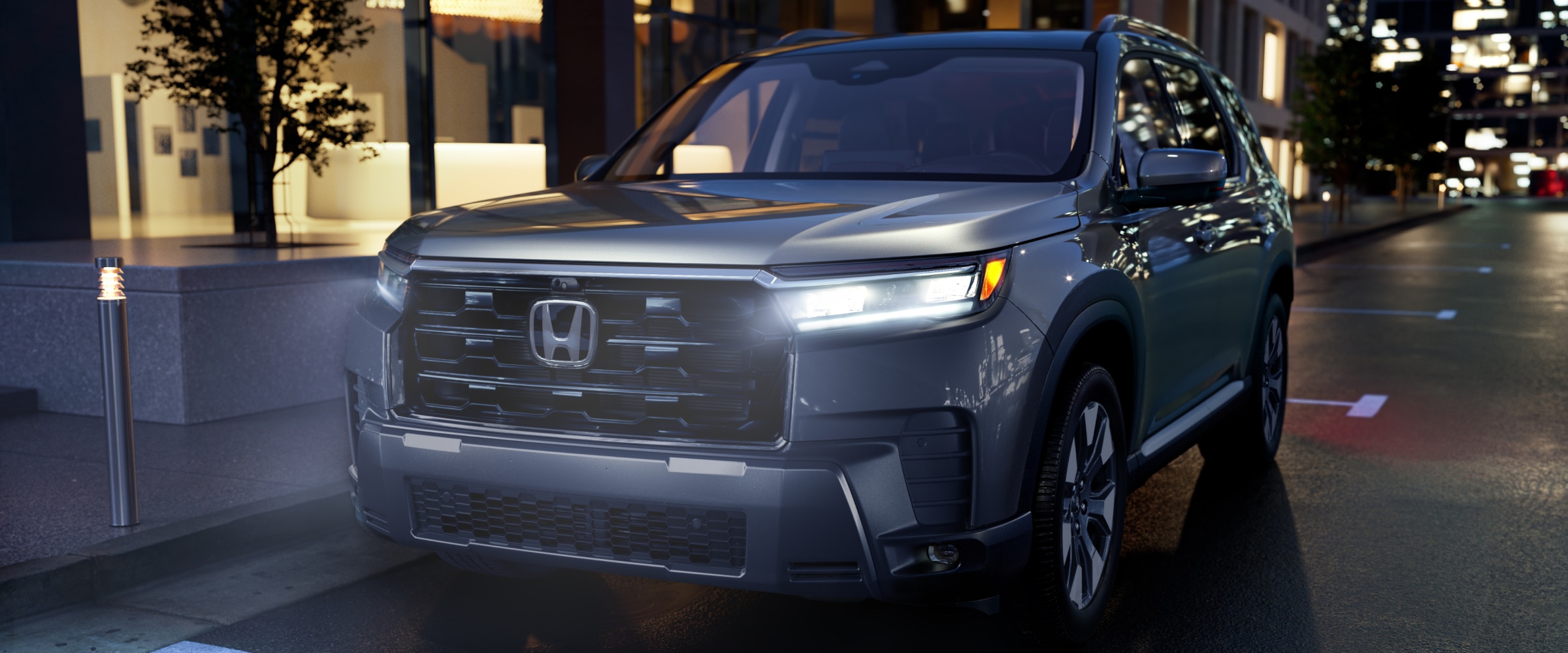 Vue de trois quarts avant d’un Pilot argenté garé en ville avec ses phares allumés.