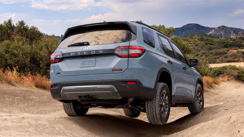 Vue de trois quarts arrière d’un Pilot bleu clair roulant sur un terrain accidenté avec des montagnes en arrière-plan.