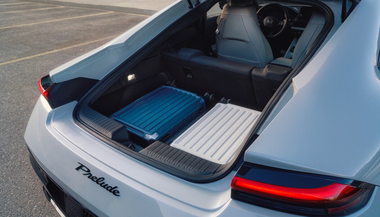 Rear view of the open trunk on a White Prelude with two hardshell suitcases inside. 