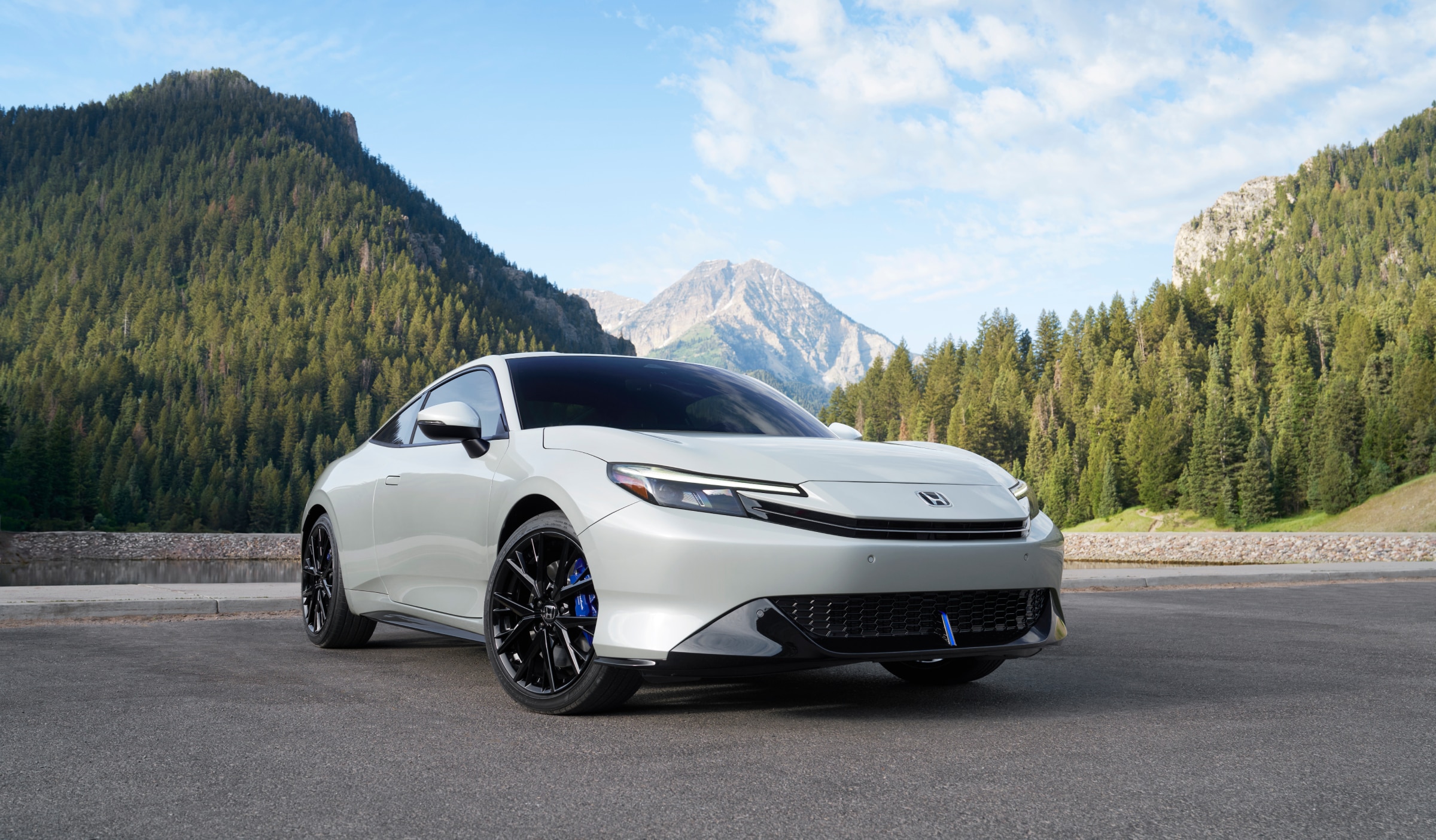 3/4 front side view of white Prelude set against a backdrop of mountains and trees.