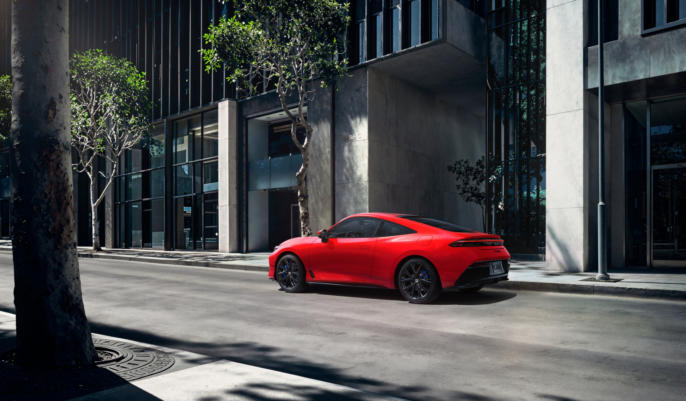 3/4 rear side view of a red Prelude driving on a tree-lined city street.