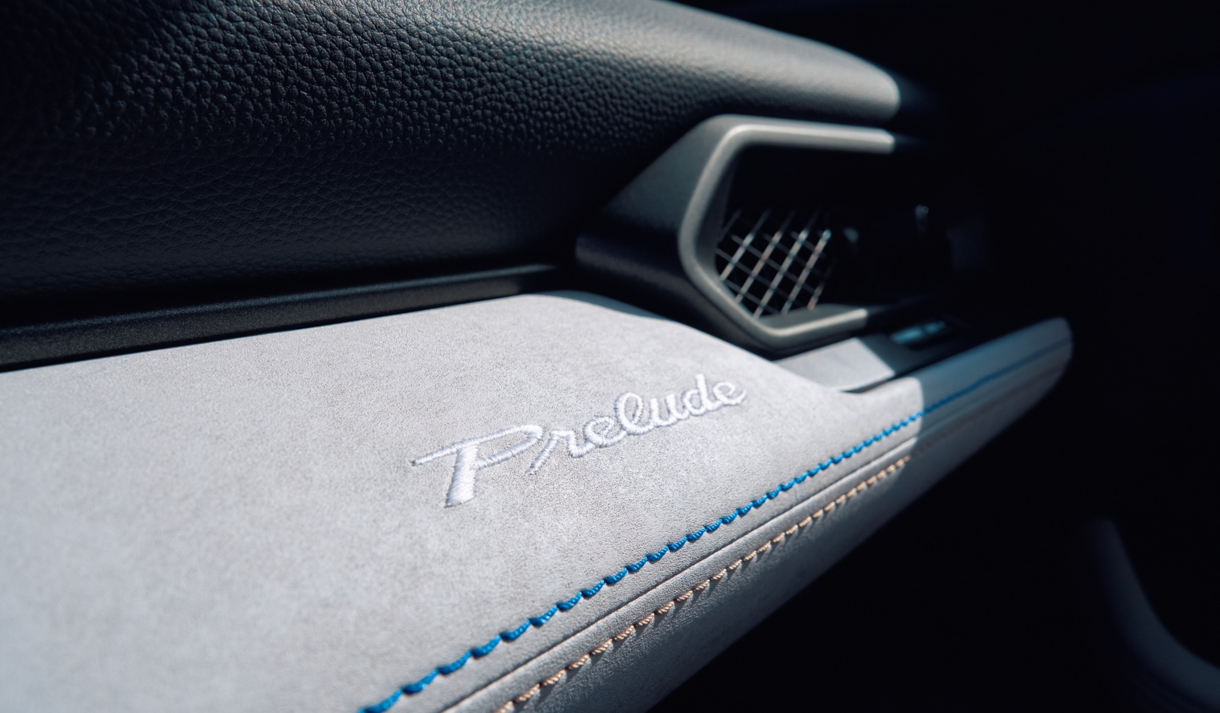 Closeup of Prelude's grey dashboard with blue and cream contrast stitching and stitched Prelude logo.