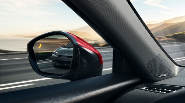 Closeup of driver's side mirror with Blind Spot alert activated and a black vehicle in the mirror's reflection. 