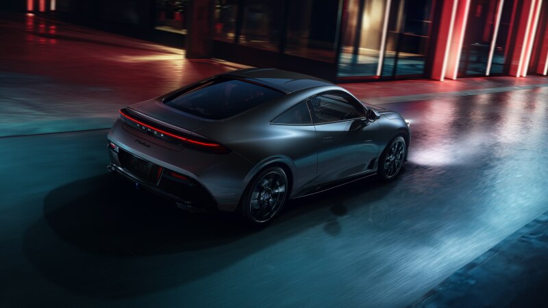 3/4 rear side view of a dark grey Prelude driving on a city street at night. 