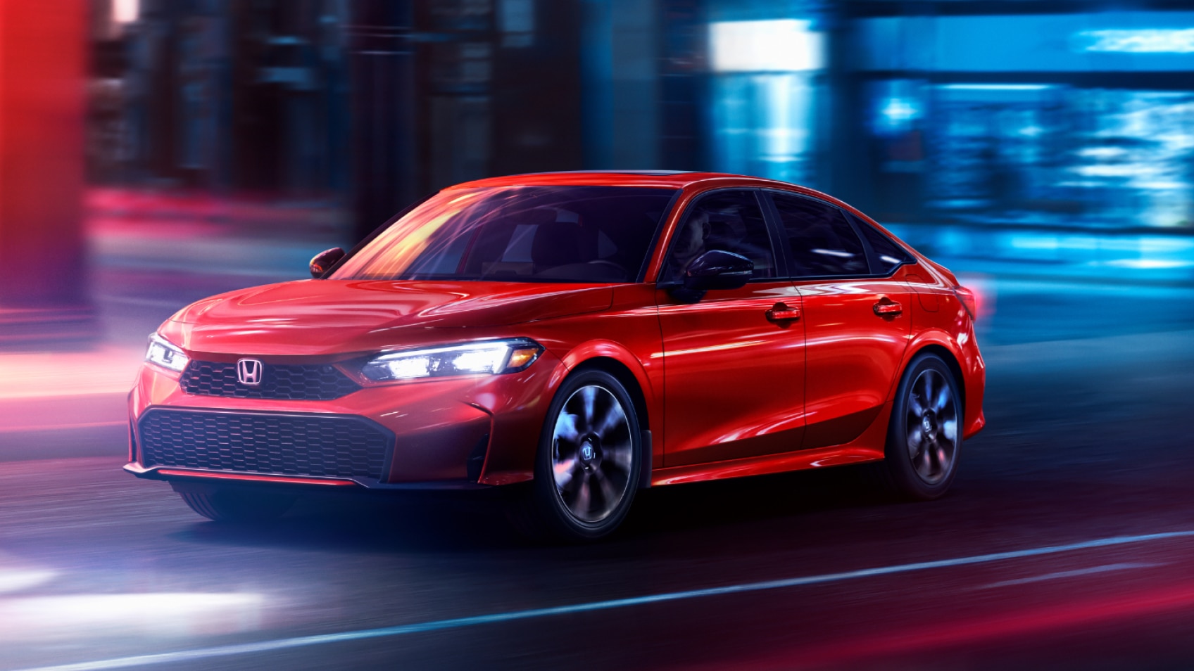 3/4 front side view of red Civic Hybrid driving on a city street at night with its headlights on.