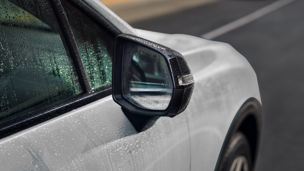 Closeup of side mirror on white Prologue covered in rain drops. 