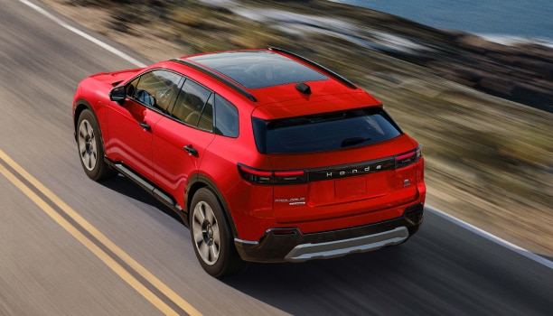 Plan en plongée de trois quarts arrière d’un Prologue rouge roulant sur une autoroute côtière.