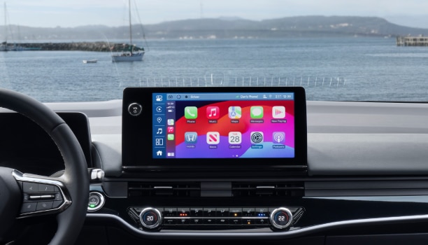 Panoramic interior view of steering wheel, front and centre consoles, and digital touchscreen. Out the windshield we see boats in the water and the Golden Gate Bridge.