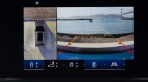 Closeup of touchscreen displaying a bird’s eye view of a Prologue in a parking spot and what the front cameras see: the curb in front, the ocean, and the Golden Gate Bridge.