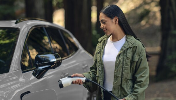View of a woman plugging in a charging cord into a white Prologue in temperate forest.
