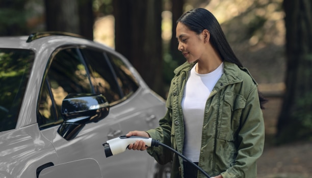 View of a woman plugging in a charging cord into a white Prologue in temperate forest.