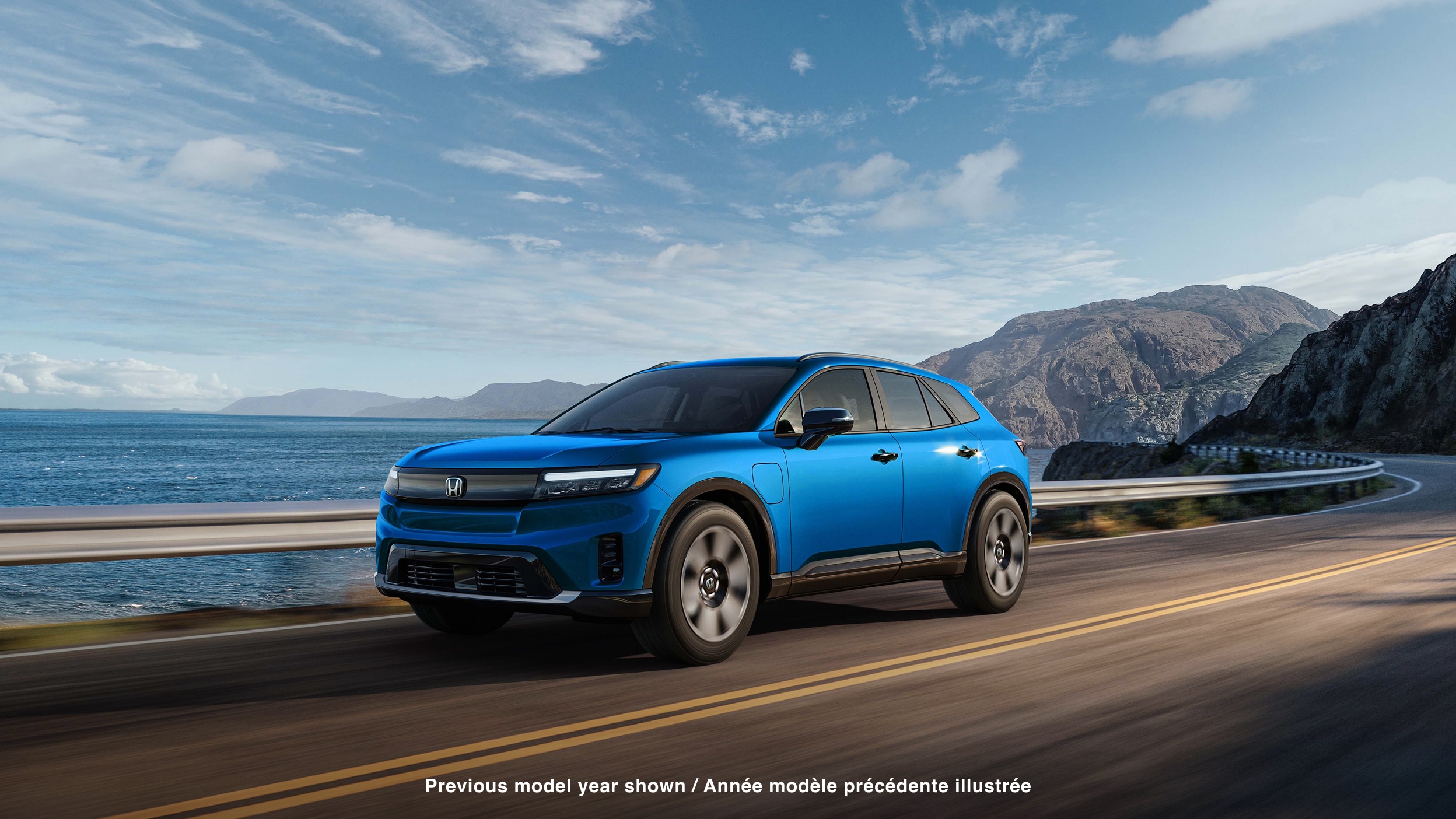 Plan large de trois quarts avant d’un Prologue bleu roulant sur une autoroute côtière avec des montagnes en arrière-plan.