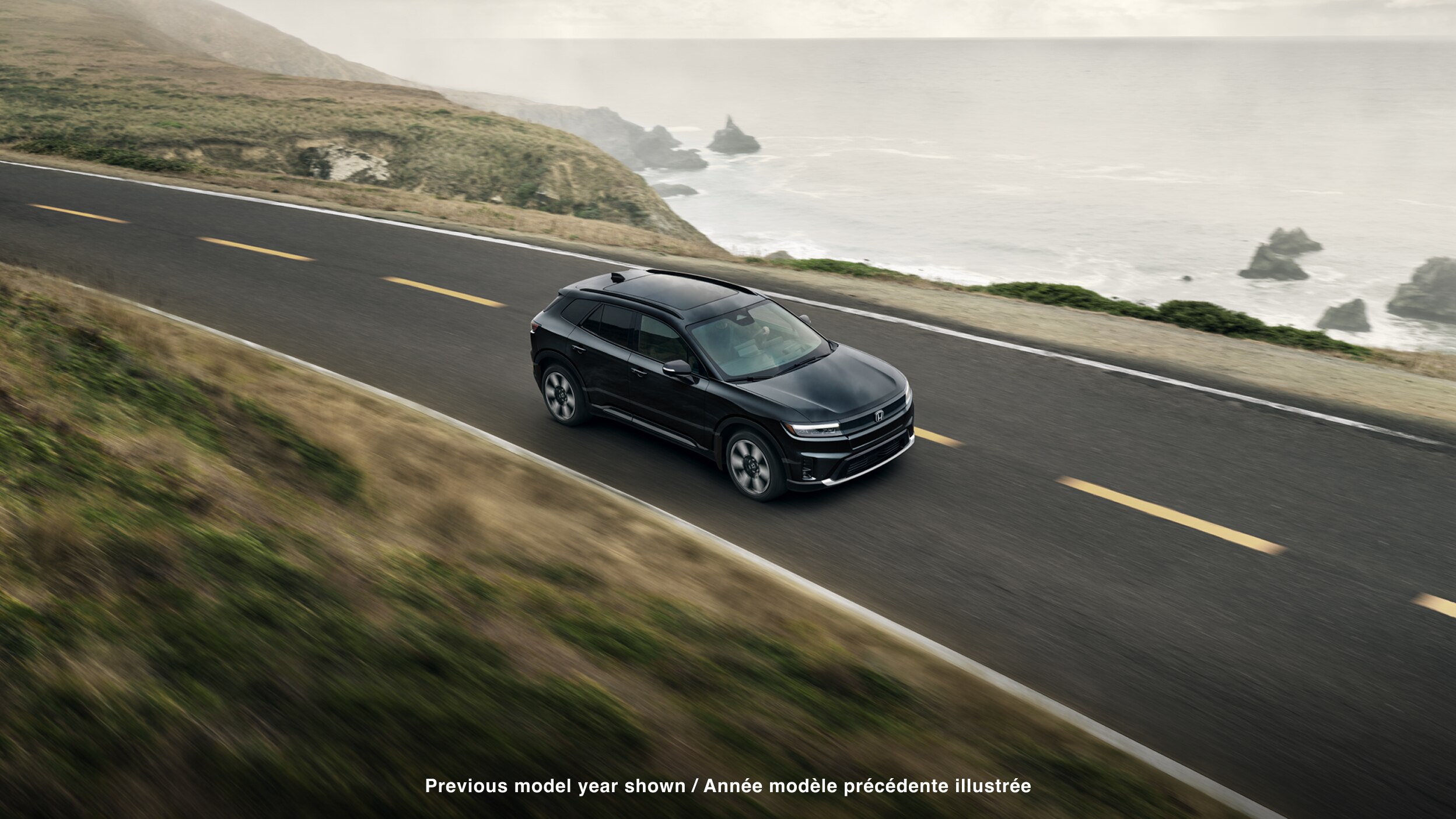 3/4 bird’s eye side view of black Prologue driving along a coastal highway.