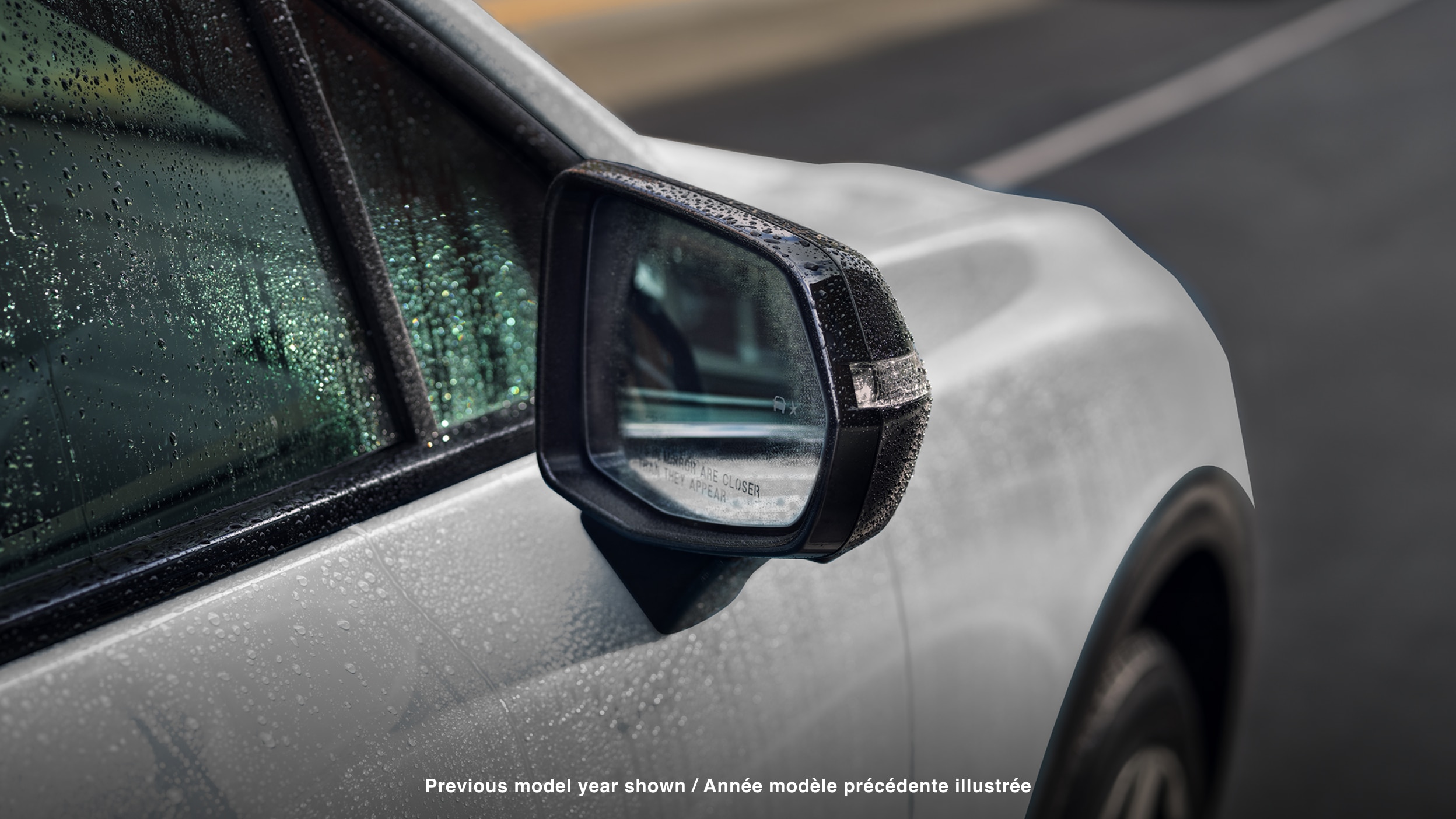 Closeup of side mirror on white Prologue covered in rain drops.