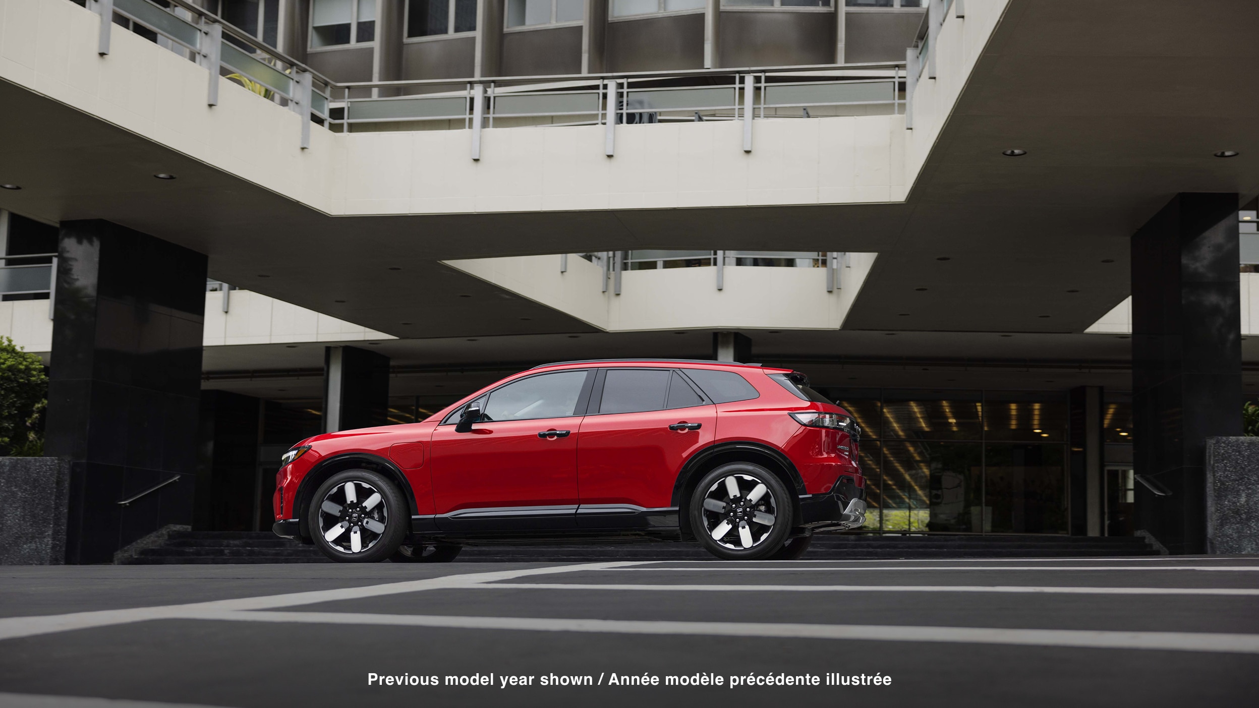 Wide side view of red Prologue parked in the driveway of a hotel-type building.