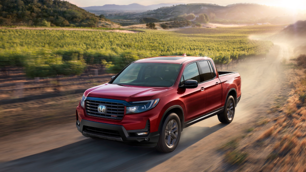 3/4 front view of red Honda Ridgeline driving on dirt round in wine country.