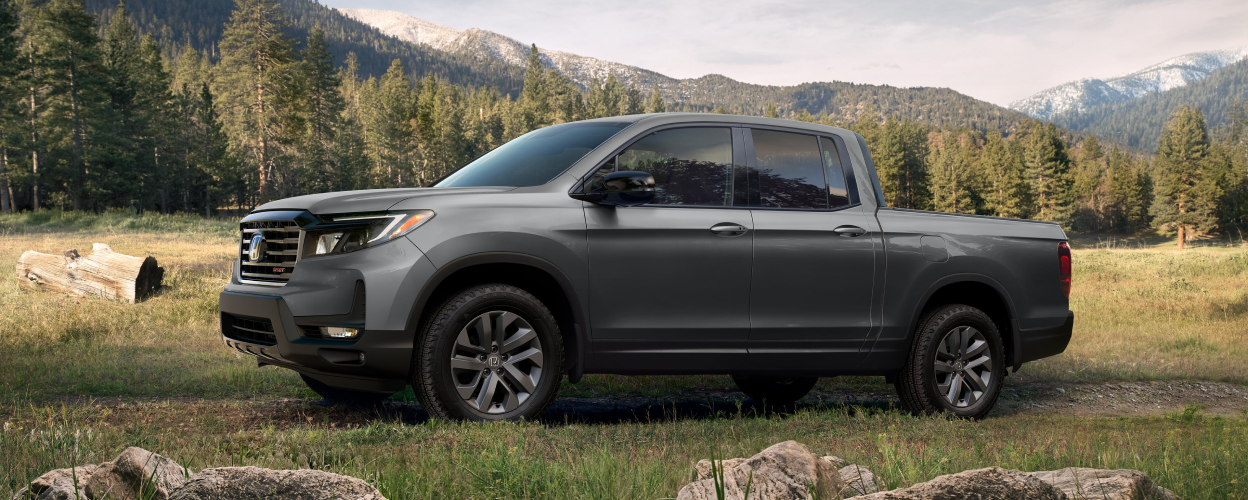 Side view of grey Honda Ridgeline in forest.