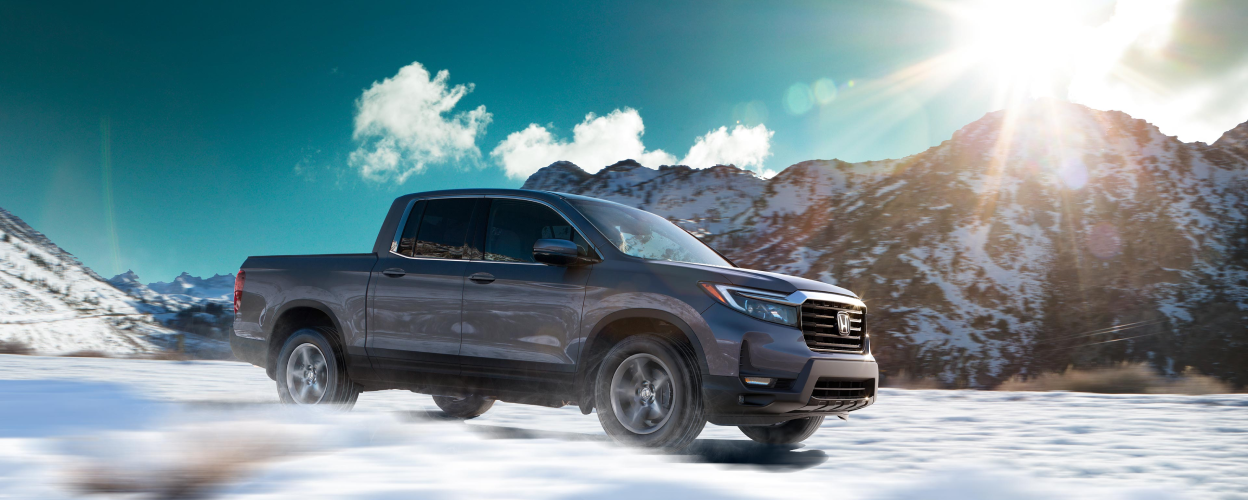 3/4 side view of Honda Ridgeline driving amid snowy mountains.