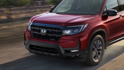 3/4 front view of red Ridgeline driving on dirt road in wine country.