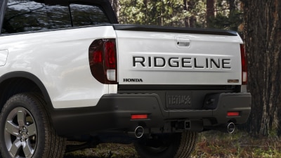 3/4 rear view of white Ridgeline parked in forest, showcasing dual exhaust.