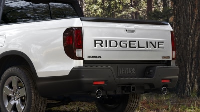Plan de trois quarts arrière d’un Ridgeline blanc stationné en forêt, présentant un échappement double.