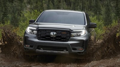 Front view of grey Ridgeline driving toward camera on muddy road, splashing mud everywhere.