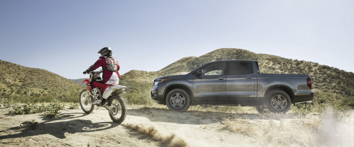 Plan latéral d’un Ridgeline gris sur des collines désertiques avec motocross à gauche.