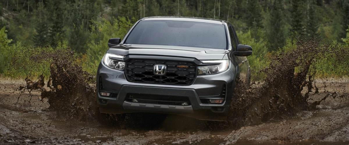 Plan avant d’un Ridgeline gris roulant vers la caméra sur une route boueuse, éclaboussant de la boue partout.