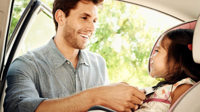 A dad buckling up his daughter in a baby car seat.