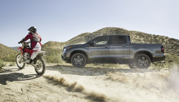 Side view of grey Ridgeline on desert hills with motocrosser on the left.