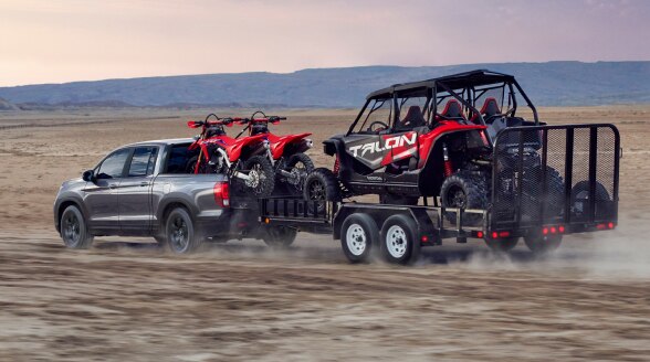 A Ridgeline hauls a trailer with motocross bikes in the desert. 