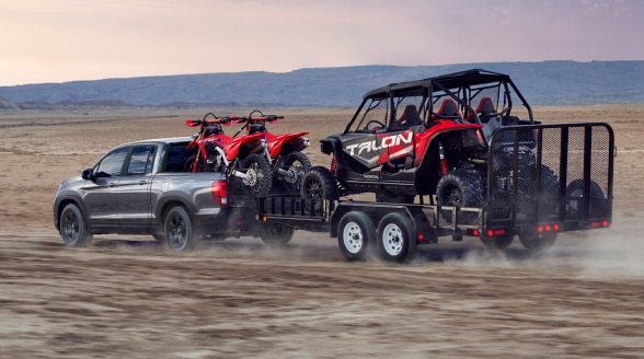 A Ridgeline hauls a trailer with motocross bikes in the desert.