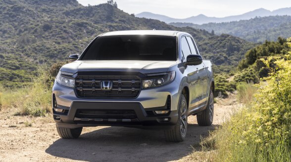 Front view of grey Ridgeline driving toward camera on muddy road, splashing mud everywhere.