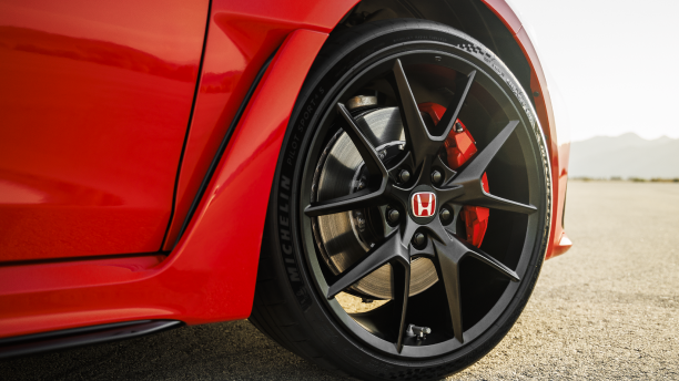 Closeup of black rimmed front wheel on a red Type R in the desert. 