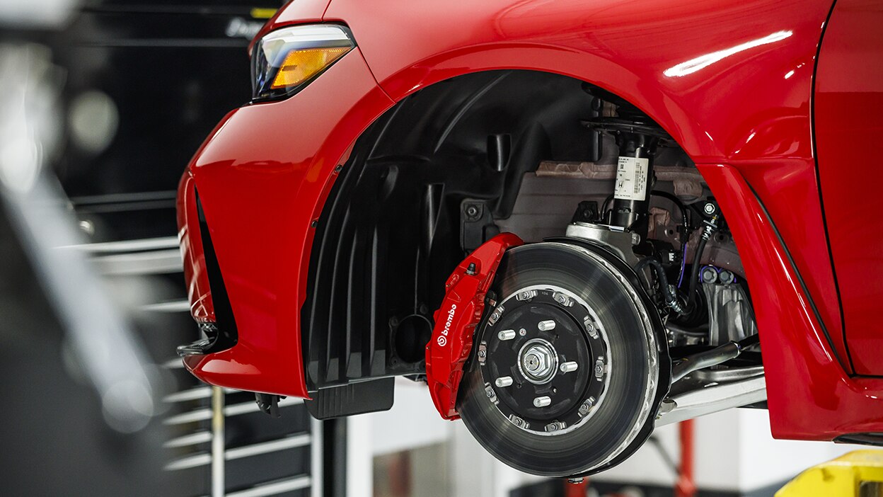 Closeup of disc brake and Brembo® caliper on red Type R on a lift in a garage.
