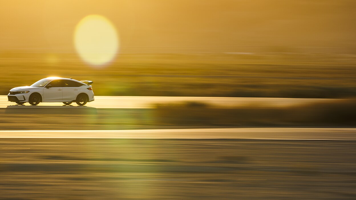 Plan d’ensemble et vue latérale d’une Type R blanche conduite sur une autoroute au coucher du soleil dans le désert. La partie avant est plus visible.