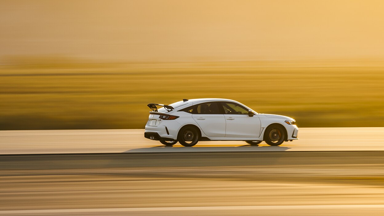 Wide shot and sideview of a white Type R driving down a highway during a desert sunset. Rear is more visible. 