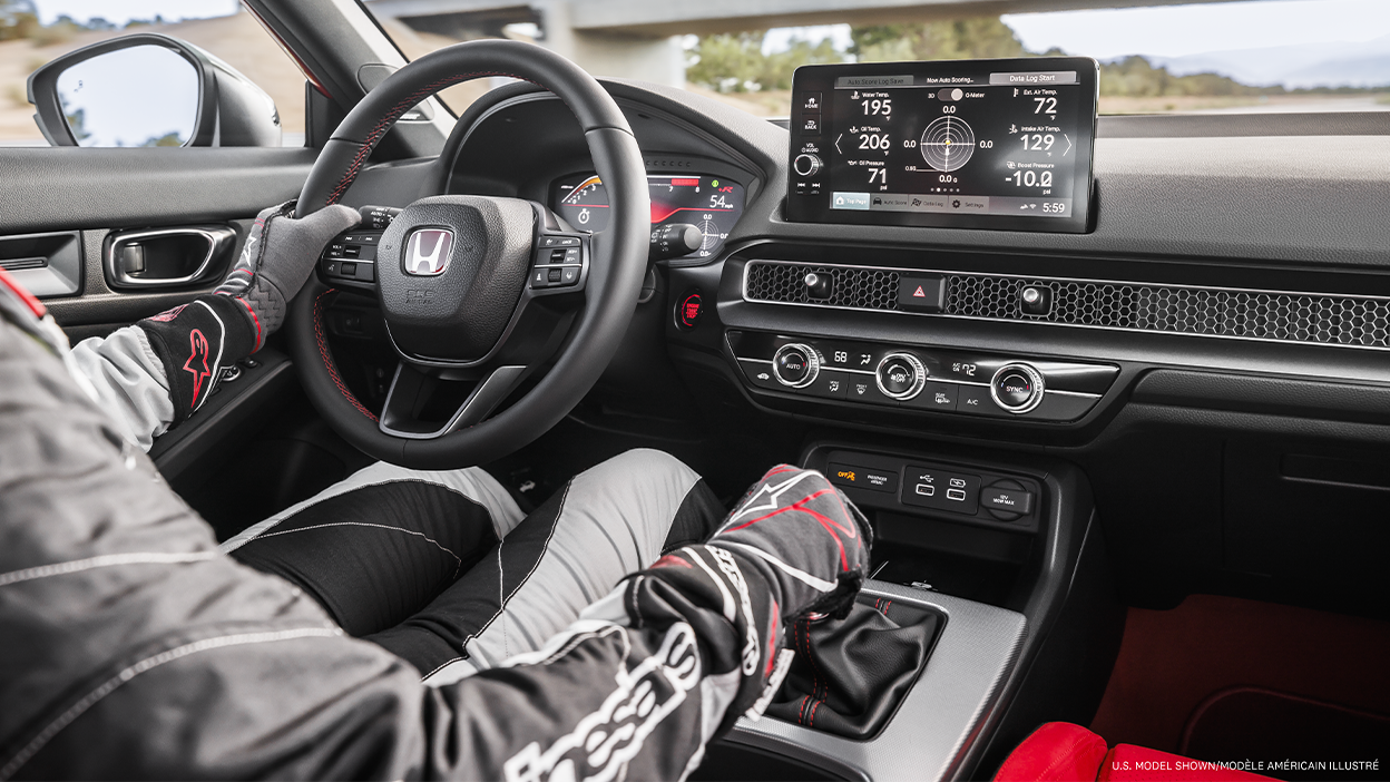 Vue intérieure d’un pilote tenant le volant, de l’habitacle de la Type R et des renseignements du système LogR à l’écran tactile.