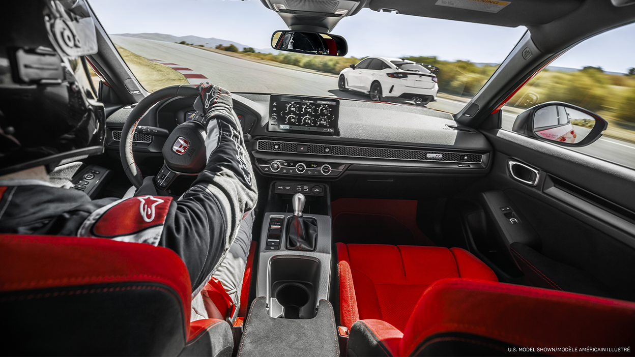 Vue intérieure, au-dessus de l’épaule du pilote, montrant le poste de pilotage de la Type R conduite sur un circuit.