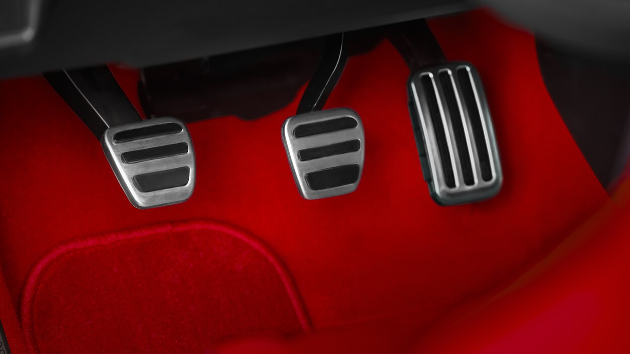 Closeup of aluminum-trimmed sport pedals and red felt footwell.