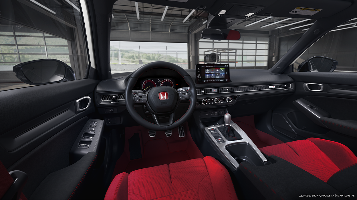 Panoramic view of steering wheel and front dashboard. Out the windshield, we see an open racing garage door. 
