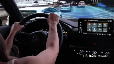 View, out windshield, over driver’s shoulder, showing Type R in traffic. Blue sensor waves emit from the front.