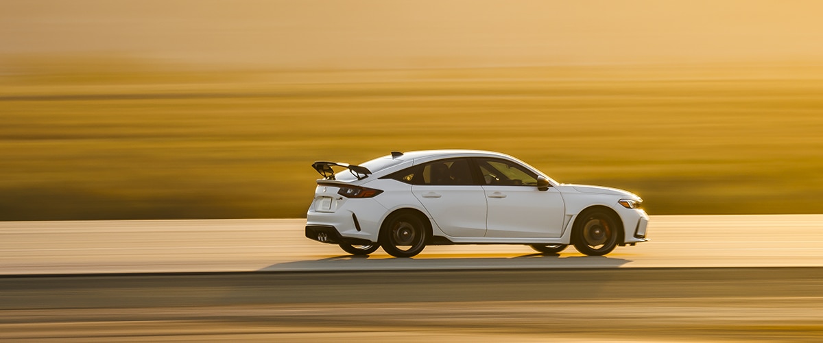 Wide shot and sideview of a white Type R driving down a highway during a desert sunset. Rear is more visible. 