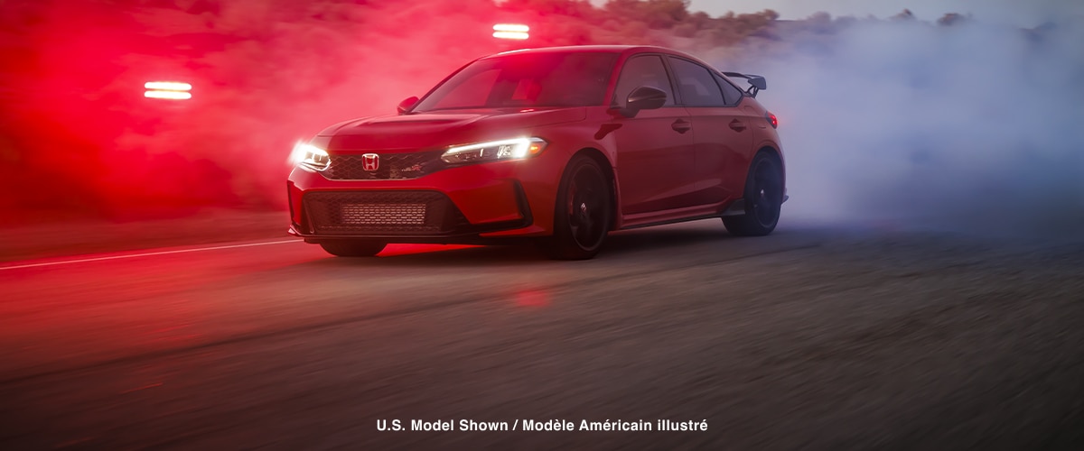 Plan de trois quarts de l’avant d’une Type R rouge qui démarre en trombe sur une route de désert à la nuit tombante.