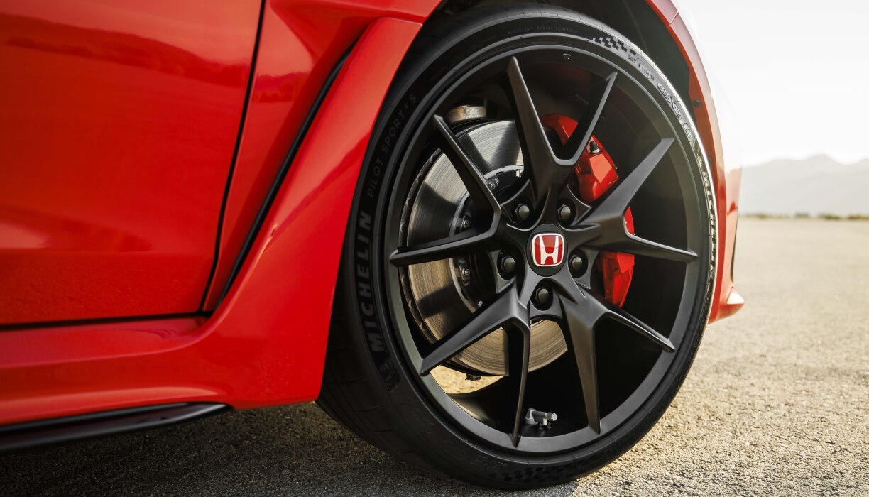 Gros plan d’une roue avant à bordure noire d’une Type R rouge dans le désert.