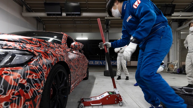 A Type R, with a funky red paint job with white Type R monograms, in a garage about to get lifted with a jack.
