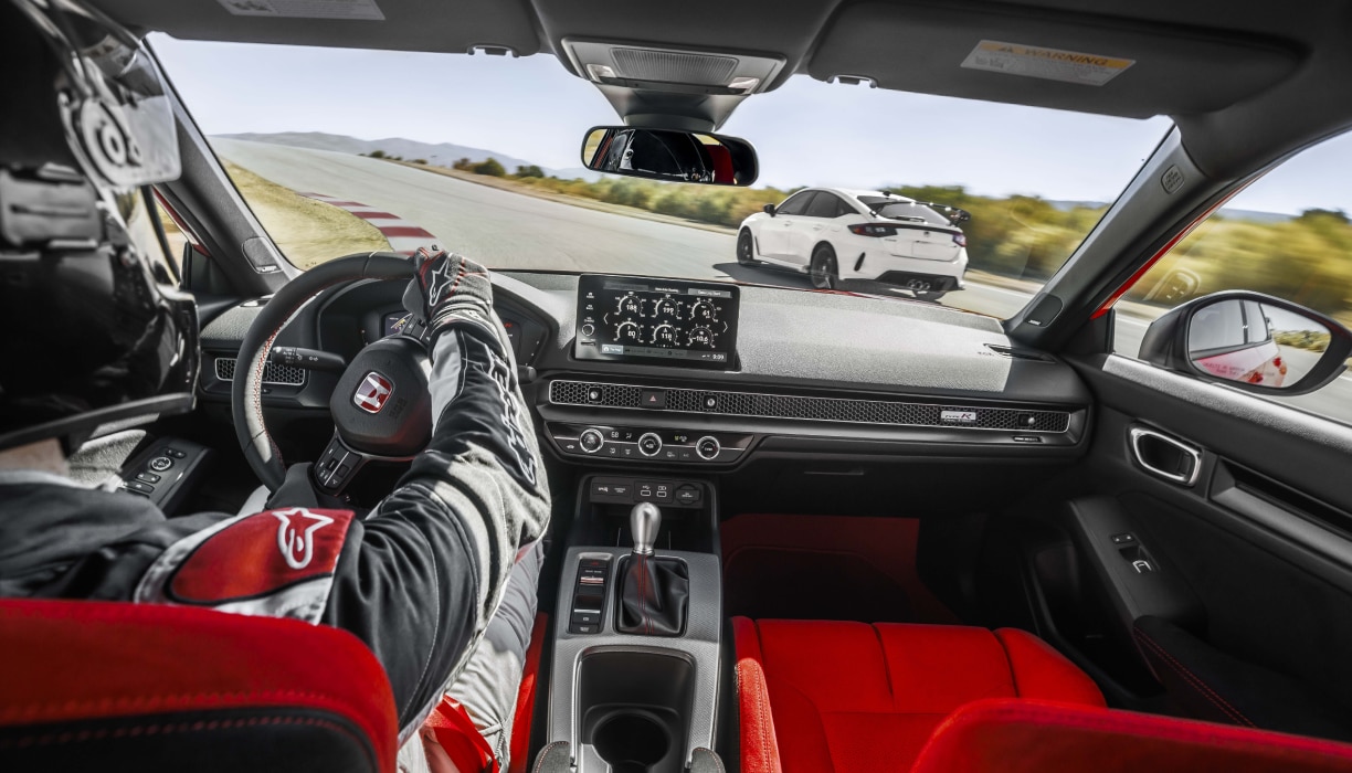 Vue intérieure, au-dessus de l’épaule du pilote, montrant le poste de pilotage de la Type R conduite sur un circuit.