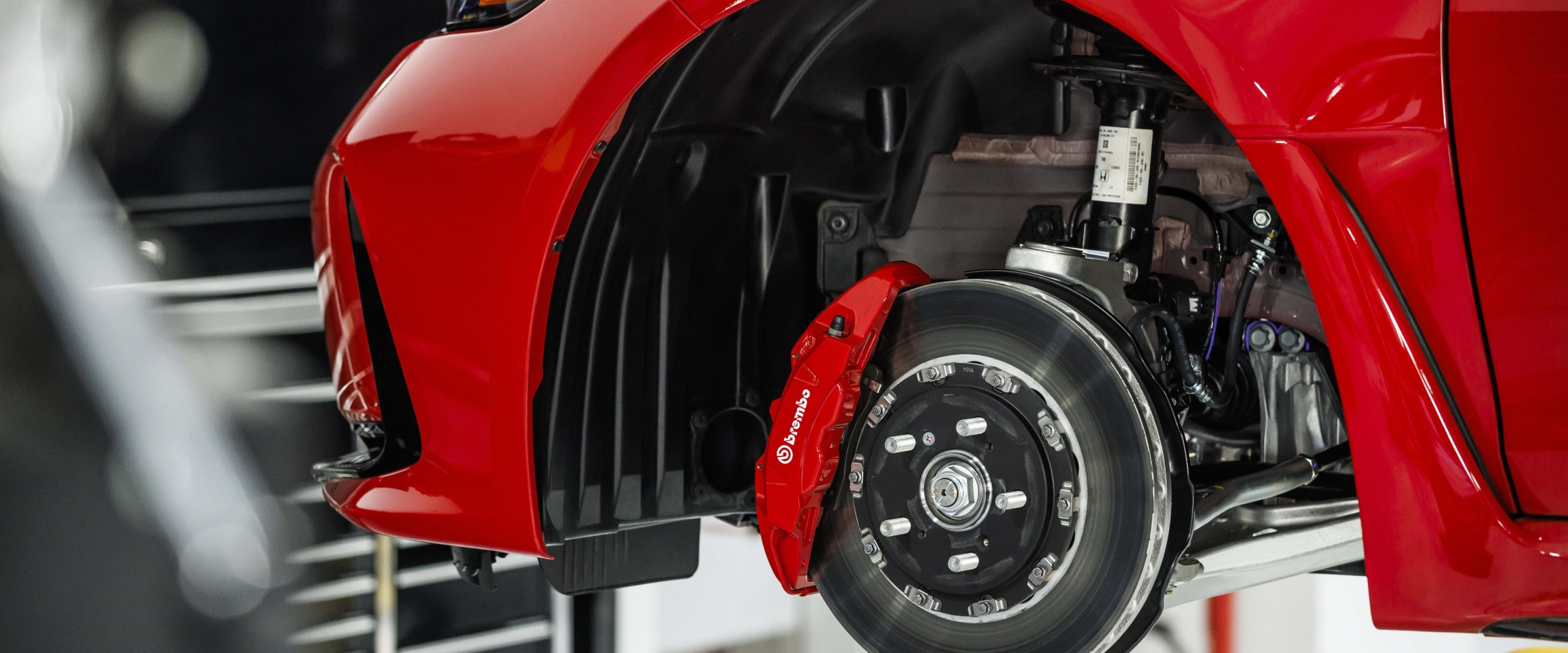 Closeup of disc brake and Brembo® caliper on red Type R on a lift in a garage.